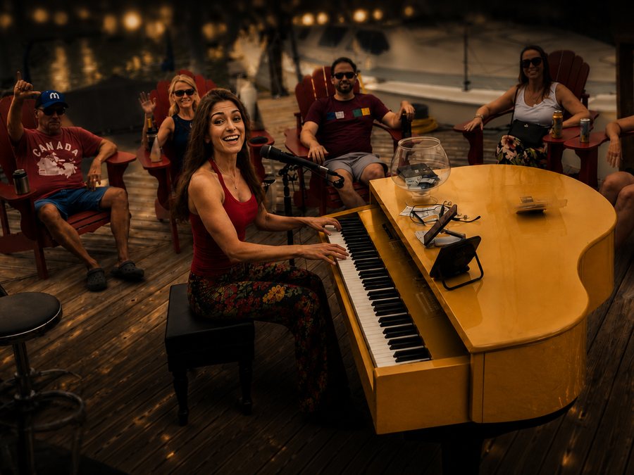 Tonya Scott playing a yellow grand piano on a marina dock with a seated audience around her